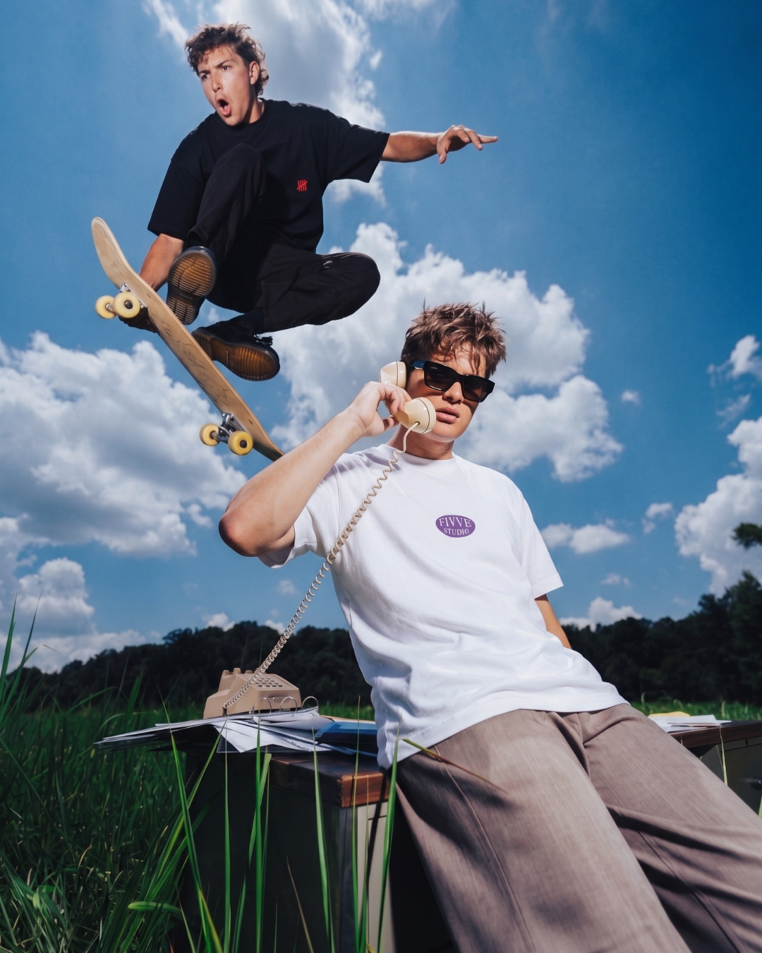 Two people with a skateboard against a blue sky with clouds